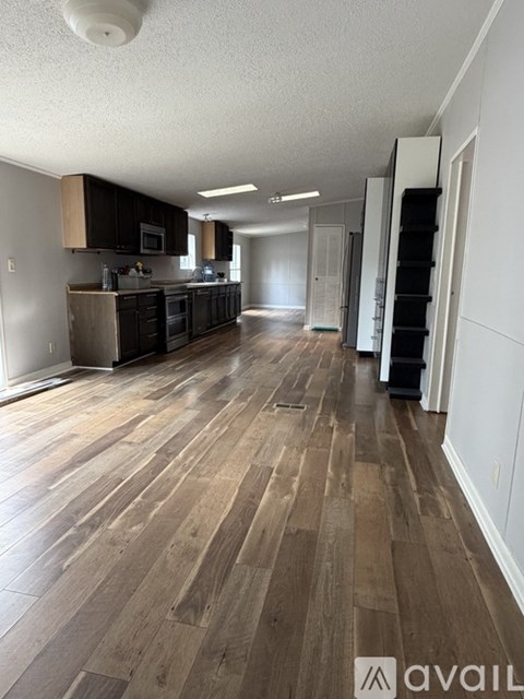 A room with wooden flooring and a kitchen area with a refrigerator, microwave, and oven.