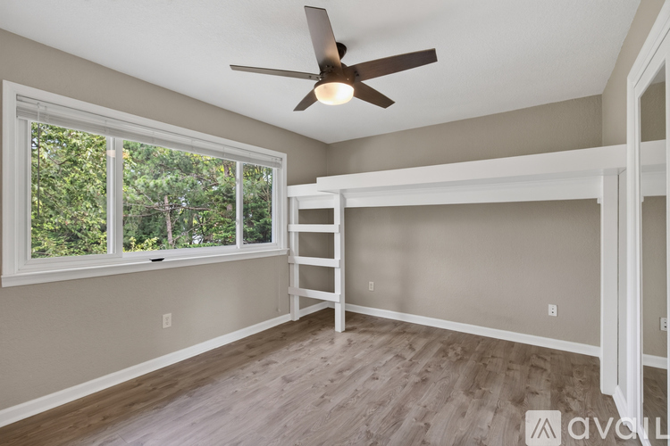 A room with a ceiling fan and a window overlooking trees.