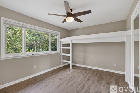 A room with a ceiling fan and a window overlooking trees.