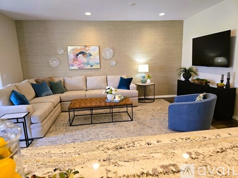 A living room with a white couch, a blue armchair, and a coffee table with a vase of flowers on it.