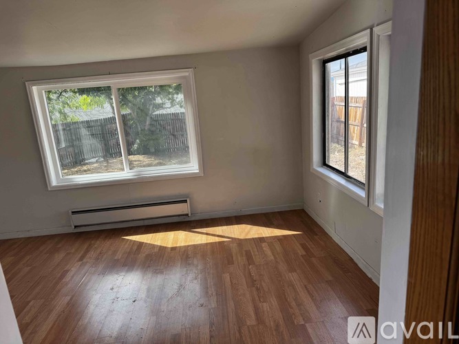 A room with wooden floors and a window with a view of a fence and trees.