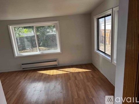 A room with wooden floors and a window with a view of a fence and trees.
