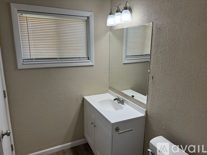 A bathroom with a sink, mirror, and window with blinds.
