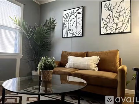 A living room with a brown couch, a glass table, and two framed artworks on the wall.