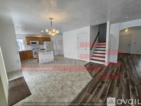 A living room with a staircase and a kitchen area in the background.