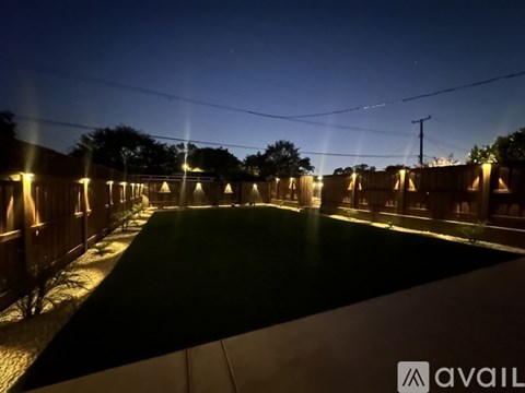A long, narrow, outdoor area with lights on the sides and a grassy field in the middle.