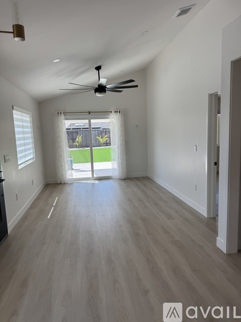 A spacious room with a ceiling fan and sliding glass doors leading to a backyard.