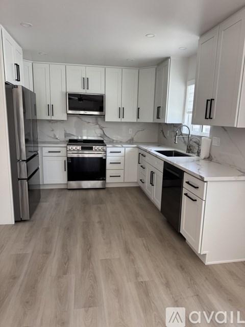 A modern kitchen with white cabinets and a wooden floor.
