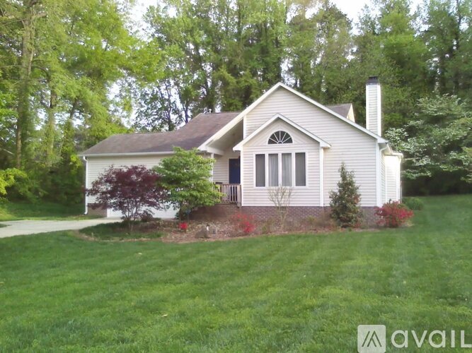 A house with a white exterior and a dark roof is surrounded by greenery.