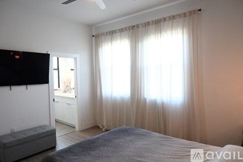 A bedroom with a bed, a television, and a window with curtains.