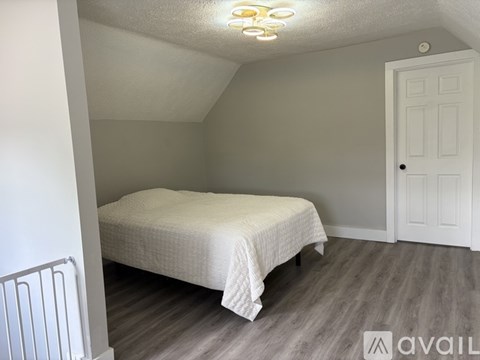 A bedroom with a bed, wooden floor, and a white door.