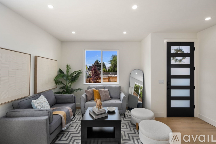 A living room with a grey couch, a coffee table, and a large window with a view of a garden.