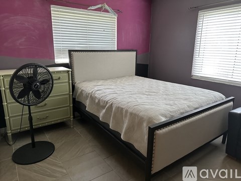 A bedroom with a bed, a fan, and a window with blinds.