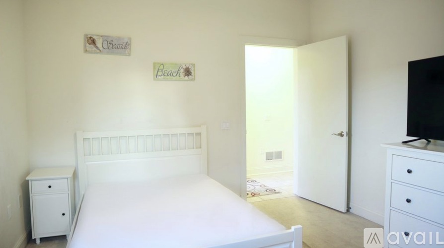 A white bedroom with a bed, nightstand, and a dresser with a television on top.