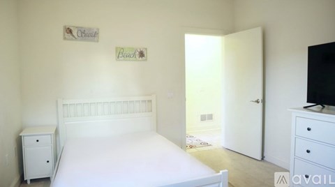 A white bedroom with a bed, nightstand, and a dresser with a television on top.