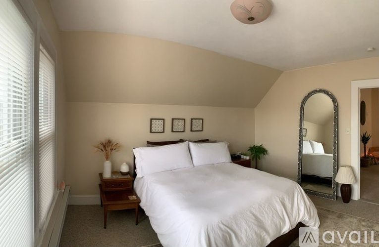 A bedroom with a large bed, a mirror, and a nightstand with a plant on it.