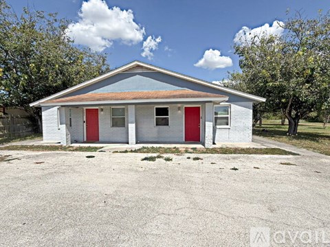 A small white house with red doors stands alone in a gravel lot.