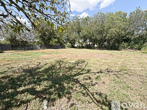 A grassy field with trees in the background and a fence on the left side.