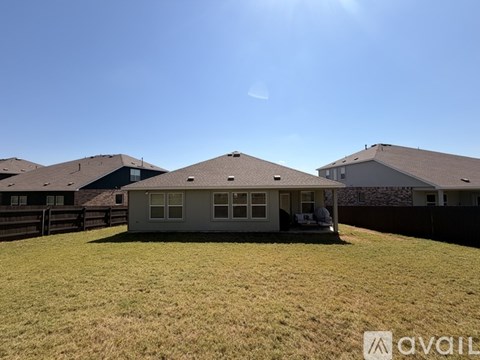 A house with a brown roof is surrounded by a grassy area and a wooden fence.