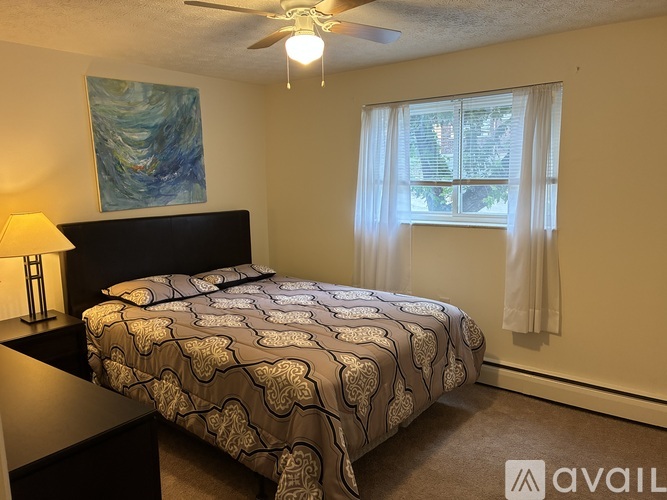 A bedroom with a bed, a ceiling fan, and a painting on the wall.