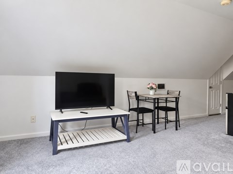 A living room with a television, a table with chairs, and a carpeted floor.