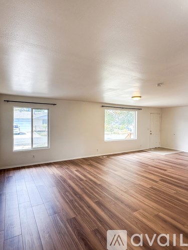 A room with wooden flooring and two windows.