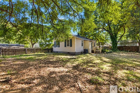 A house is surrounded by trees and has a fence in front of it.