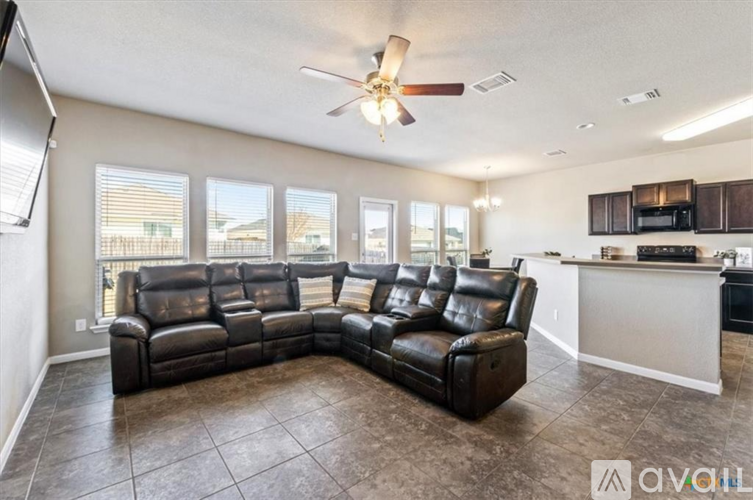 A spacious living room with a black leather sofa and a kitchen area in the background.