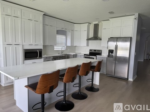 A kitchen with white cabinets and a white island with three chairs.