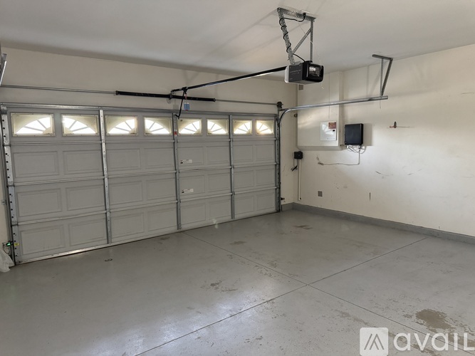 A spacious garage with a white floor and walls, equipped with overhead lighting and a garage door opener.