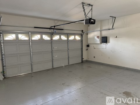 A spacious garage with a white floor and walls, equipped with overhead lighting and a garage door opener.