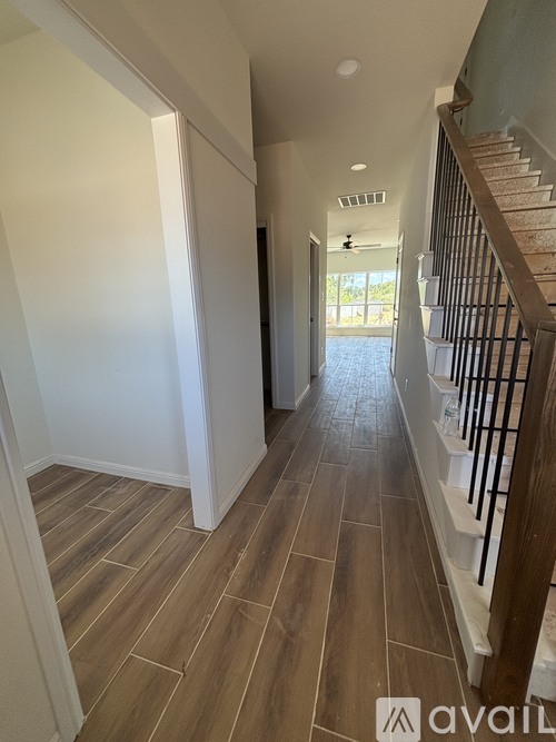 A hallway with wooden floors and a staircase on the right.