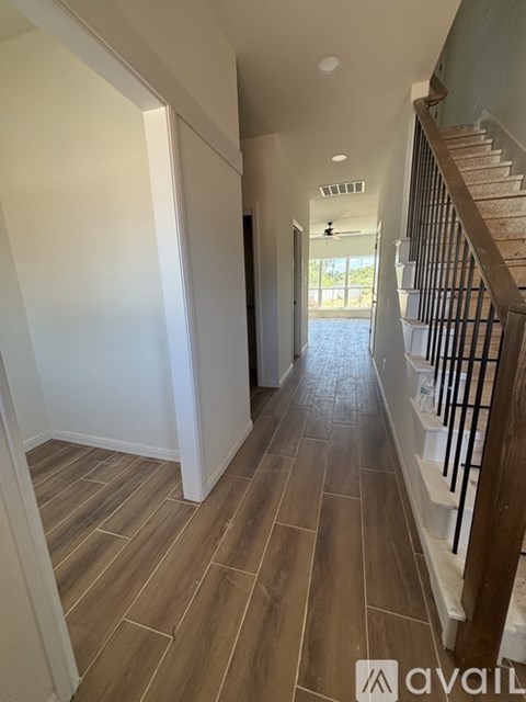 A hallway with wooden floors and a staircase on the right.