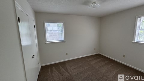 A room with a carpeted floor, a window with blinds, and a door with a black handle.