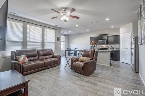 A living room with a brown leather couch and a brown leather chair with a white cabinet and a fan in the background.
