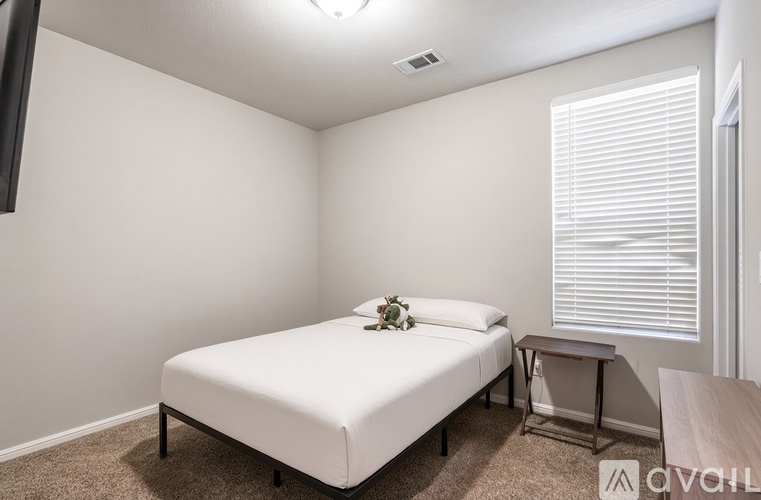 A bedroom with a white bed and a small table with a vase of flowers on it.
