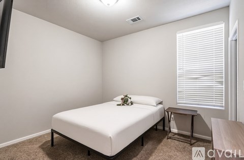 A bedroom with a white bed and a small table with a vase of flowers on it.