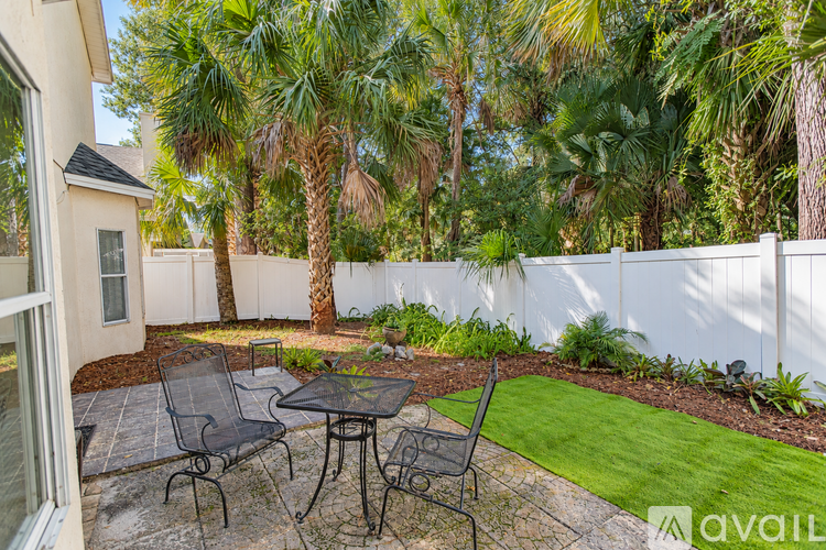 A patio with a table and chairs surrounded by a white fence and palm trees.