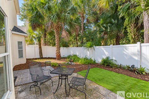 A patio with a table and chairs surrounded by a white fence and palm trees.