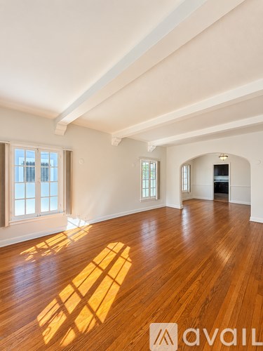 A room with wooden floors and white walls, with sunlight streaming in through the windows.