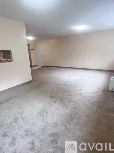 A room with a white wall and a window on the left side.