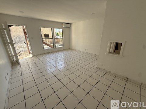 A spacious room with white tiled flooring and a large window overlooking a parking lot.