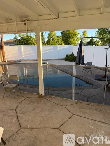 A pool enclosed by a white fence with a chair and umbrella nearby.