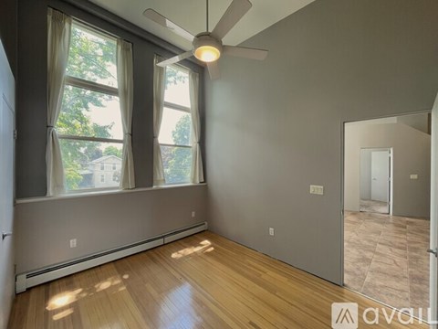 A room with a ceiling fan and a window with a view of trees.
