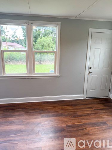 A room with a white door and a window with a view of a green lawn and trees.