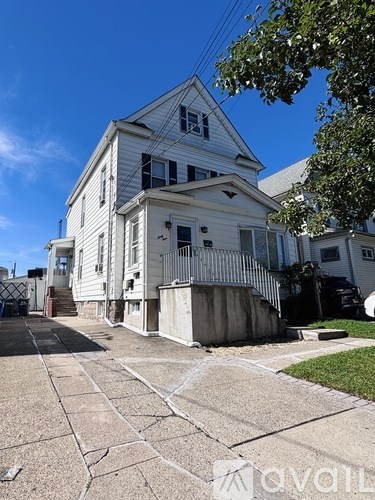 A white house with a grey front porch and a tree in front.