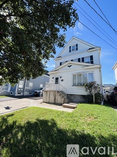 A two-story house with a white exterior and a tree in the foreground.