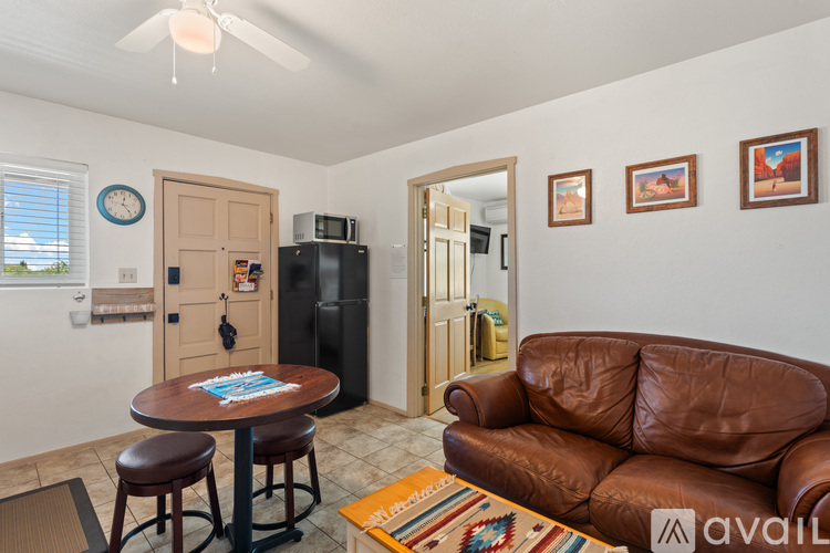 A living room with a brown leather couch and a round wooden table with two stools.