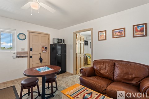 A living room with a brown leather couch and a round wooden table with two stools.