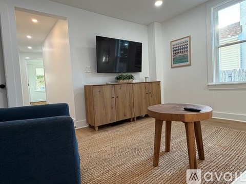 A living room with a blue chair, a wooden table, and a television on a wooden cabinet.